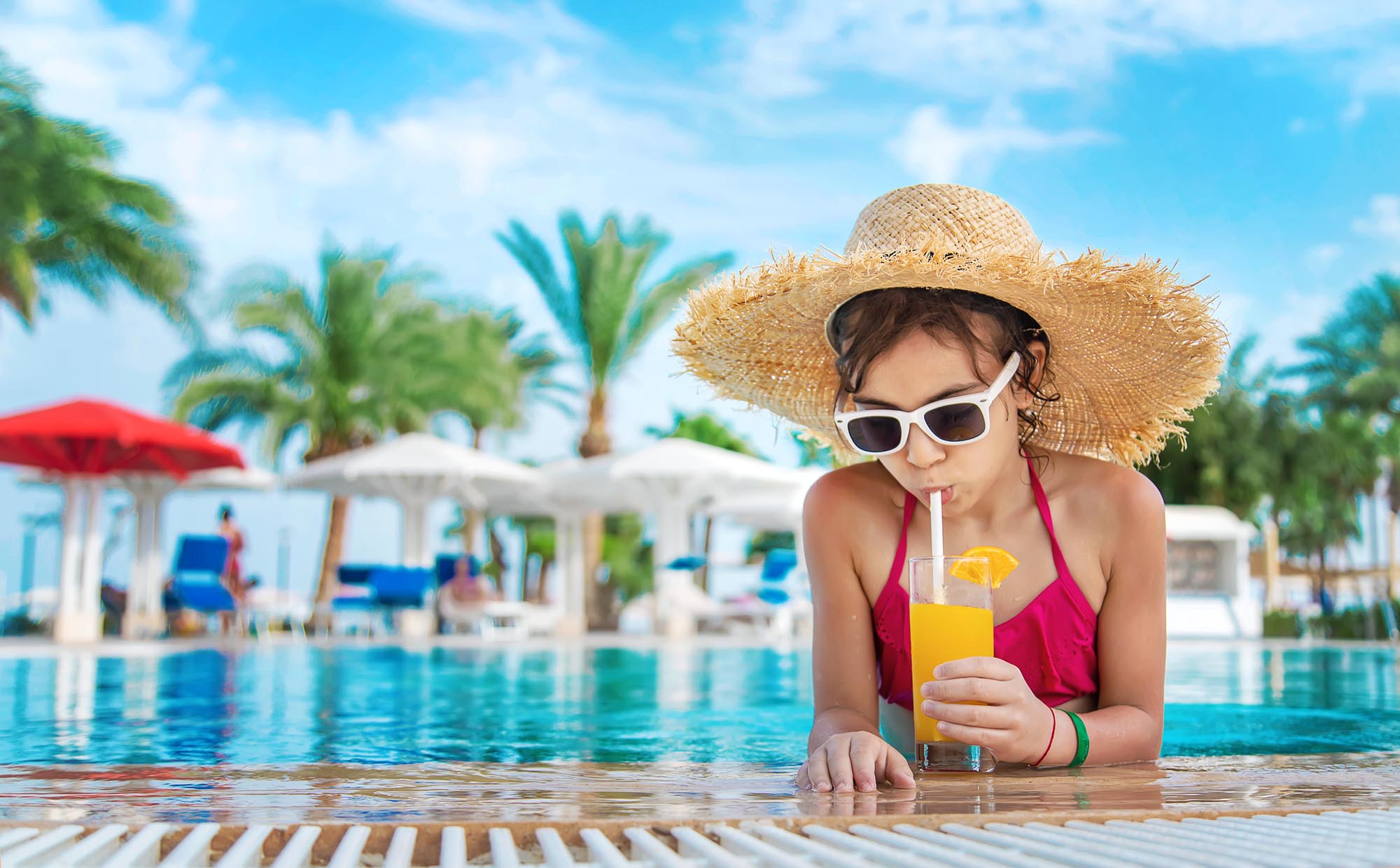 Mädchen trinkt Saft am Poolrand unter Sonnenbrillen